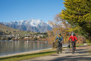 Two Electric Bike Riders at Kelvin heights beach with Remarkables in the background in Queenstown.